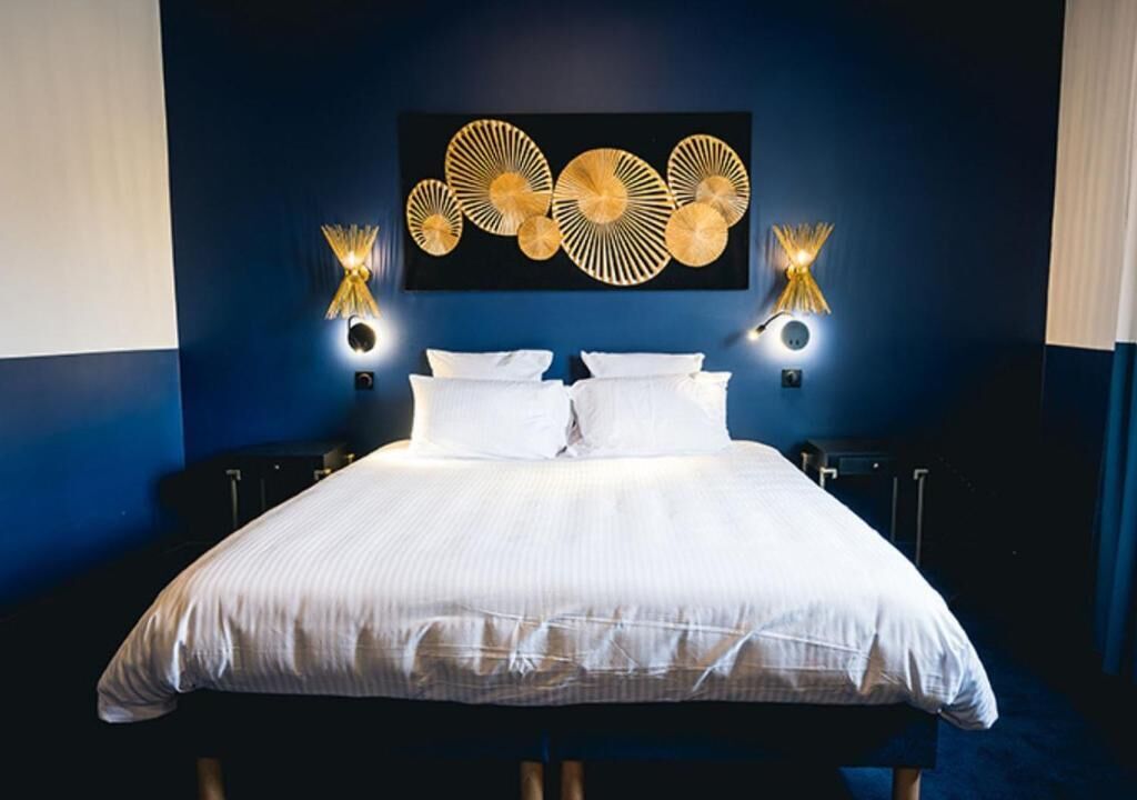 A hotel room with a large bed, two bedside tables, wall-mounted lamps, and a decorative wall piece.