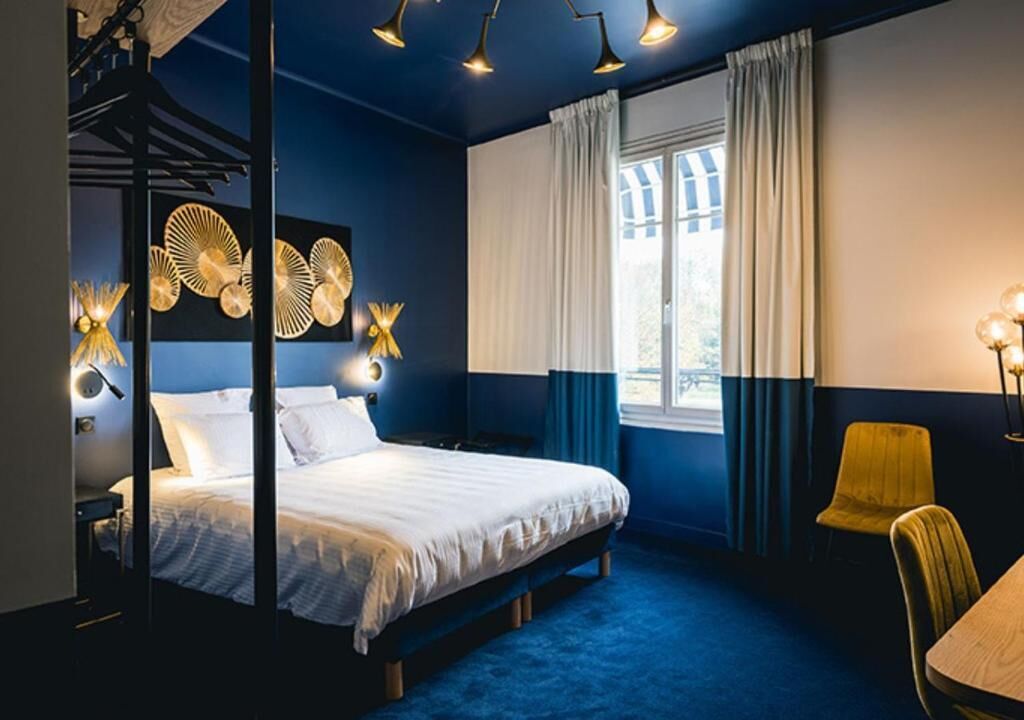 A bedroom with a bed, a desk, a chair, a window with curtains, and wall-mounted lights.