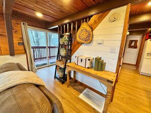 Ein gemütliches Cabin-Interieur mit Holzbalkendecke, einer Treppe, einer Bank mit Koffern, einem Regal mit Dekoration und einem großen Fenster.