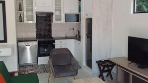 Una cocina moderna con microondas, horno y lavavajillas. En la sala de estar, hay un sofá gris y una mesa de madera.