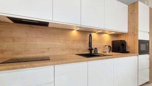 Une cuisine moderne avec des armoires blanches, un plan de travail en bois, un robinet noir, une machine à café et un four à micro-ondes.