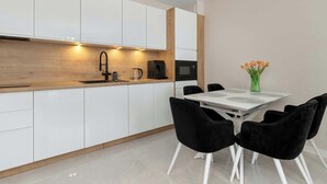 Une cuisine moderne avec des meubles blancs, un plan de travail en bois, une machine à café noire et un coin repas comprenant une table blanche et des chaises noires.