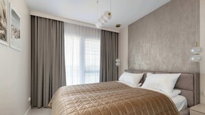 Une chambre à coucher avec un grand lit, une tête de lit, une table de chevet et une fenêtre avec des rideaux.