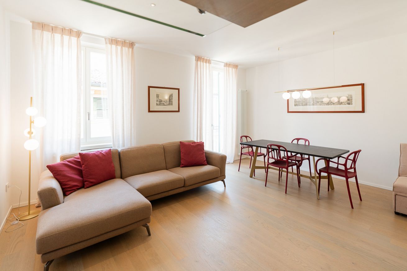 Un soggiorno moderno con un divano ad angolo beige, un tavolo da pranzo con sedie rosse e due quadri appesi alle pareti.