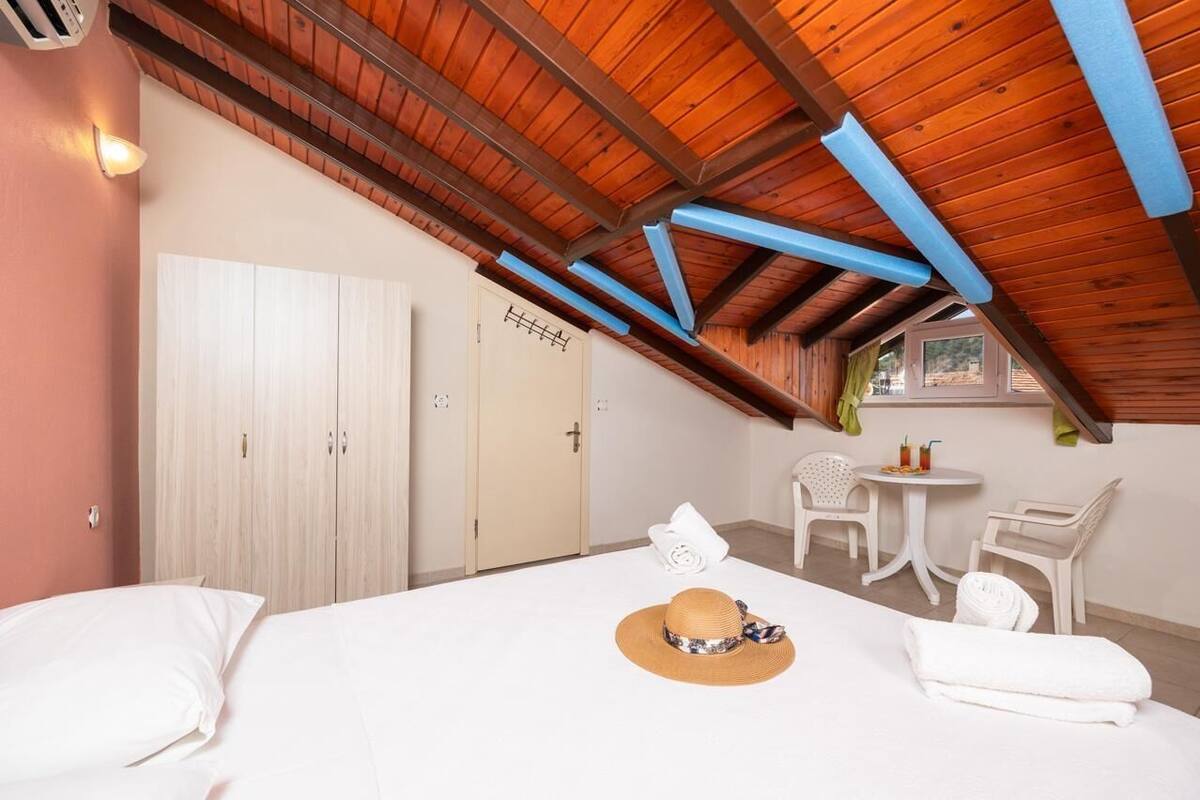 Une chambre avec un plafond en bois, un lit, une chaise, une petite table et une fenêtre.