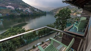 A balcony with a view of a river and hillside buildings. - Sojourn By the Lake - Boutique Hotel  (Bhimtal)