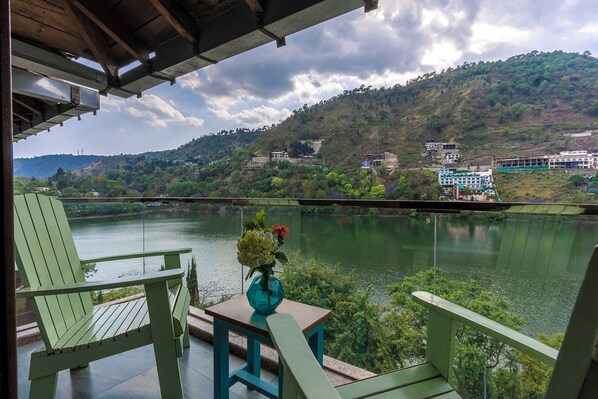 A view from a balcony overlooking a river, with a chair and a table in the foreground. - Sojourn By the Lake - Boutique Hotel (Bhimtal)