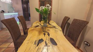Una mesa de comedor de madera con sillas de mimbre, un florero con flores y un mostrador de recepción con un letrero.