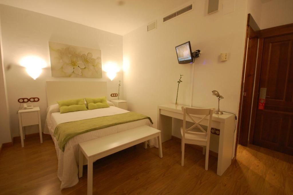 A bedroom with a bed, bedside tables, a desk, a chair, a TV, and a door.