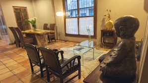 A dining area with a wooden table, chairs, a glass-top coffee table, and a statue. - Hotel HC Zoom (Pozoblanco)