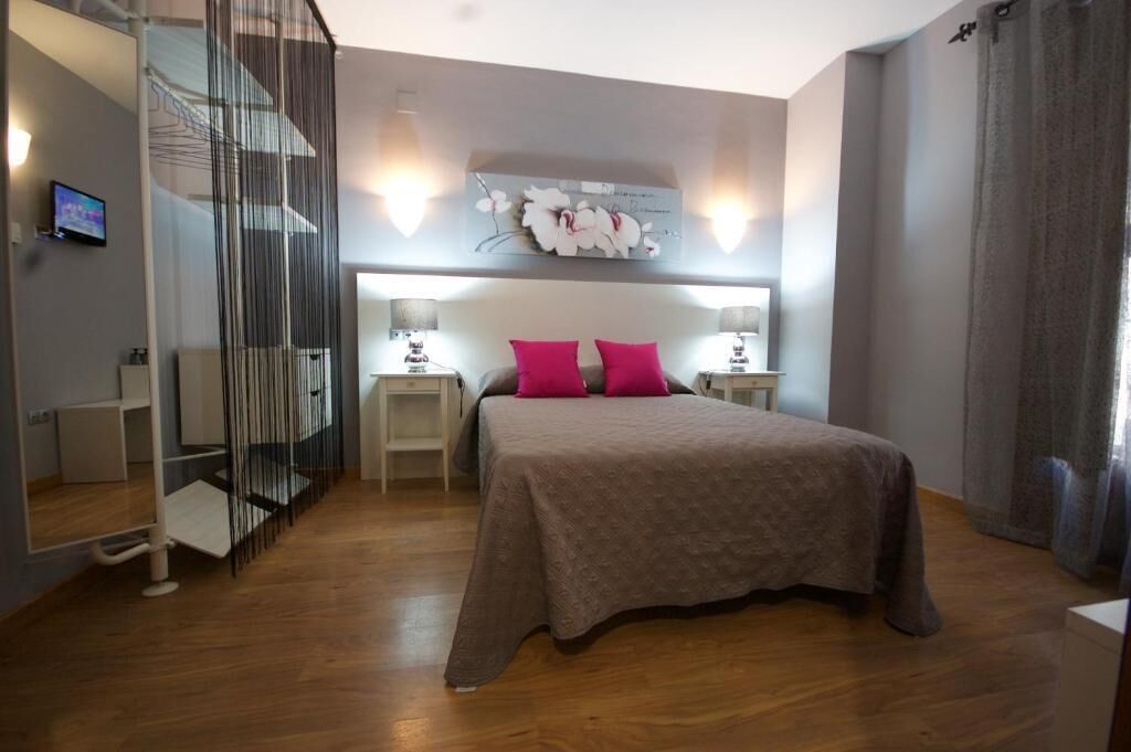 A bedroom with a bed, two bedside tables, a wall-mounted artwork, and a staircase.