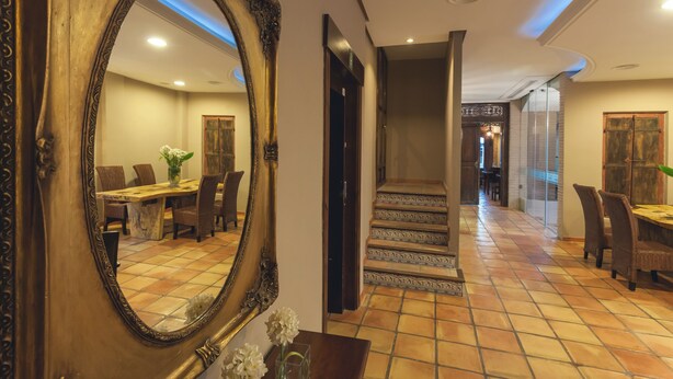 A hotel lobby with a large ornate mirror, a dining area with chairs and a table, and a staircase leading to another level. - Hotel HC Zoom (Pozoblanco)