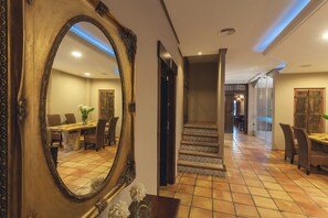 A hotel lobby with a large ornate mirror, a dining area with chairs and a table, and a staircase leading to another level. - Hotel HC Zoom (Pozoblanco)