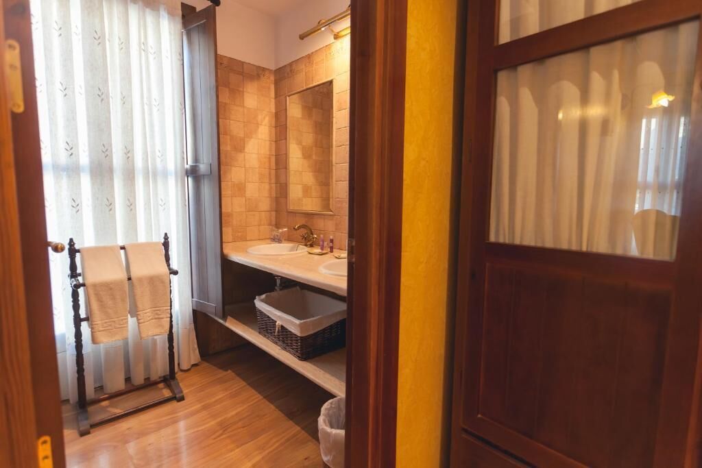 Un baño con piso de madera, un perchero con toallas, un lavamanos y un espejo.