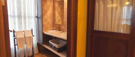 Un baño con piso de madera, un perchero con toallas, un lavamanos y un espejo.