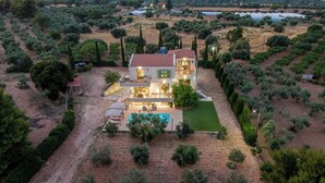 Uma casa de dois andares com piscina, rodeada por oliveiras e um gramado bem cuidado.