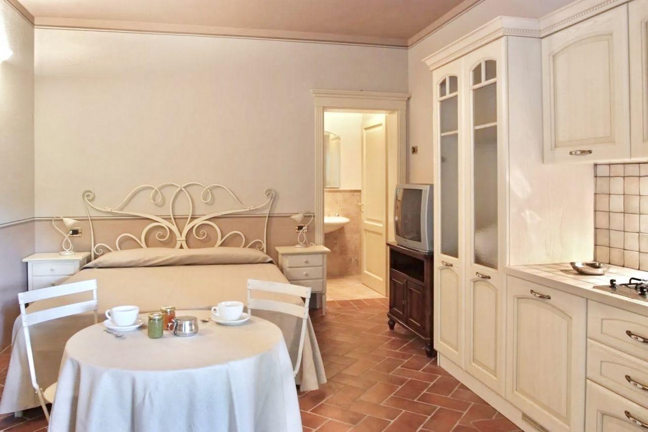 Une chambre à coucher comprenant un lit, des tables de chevet, une table ronde avec des chaises, un téléviseur et un coin cuisine avec des placards.