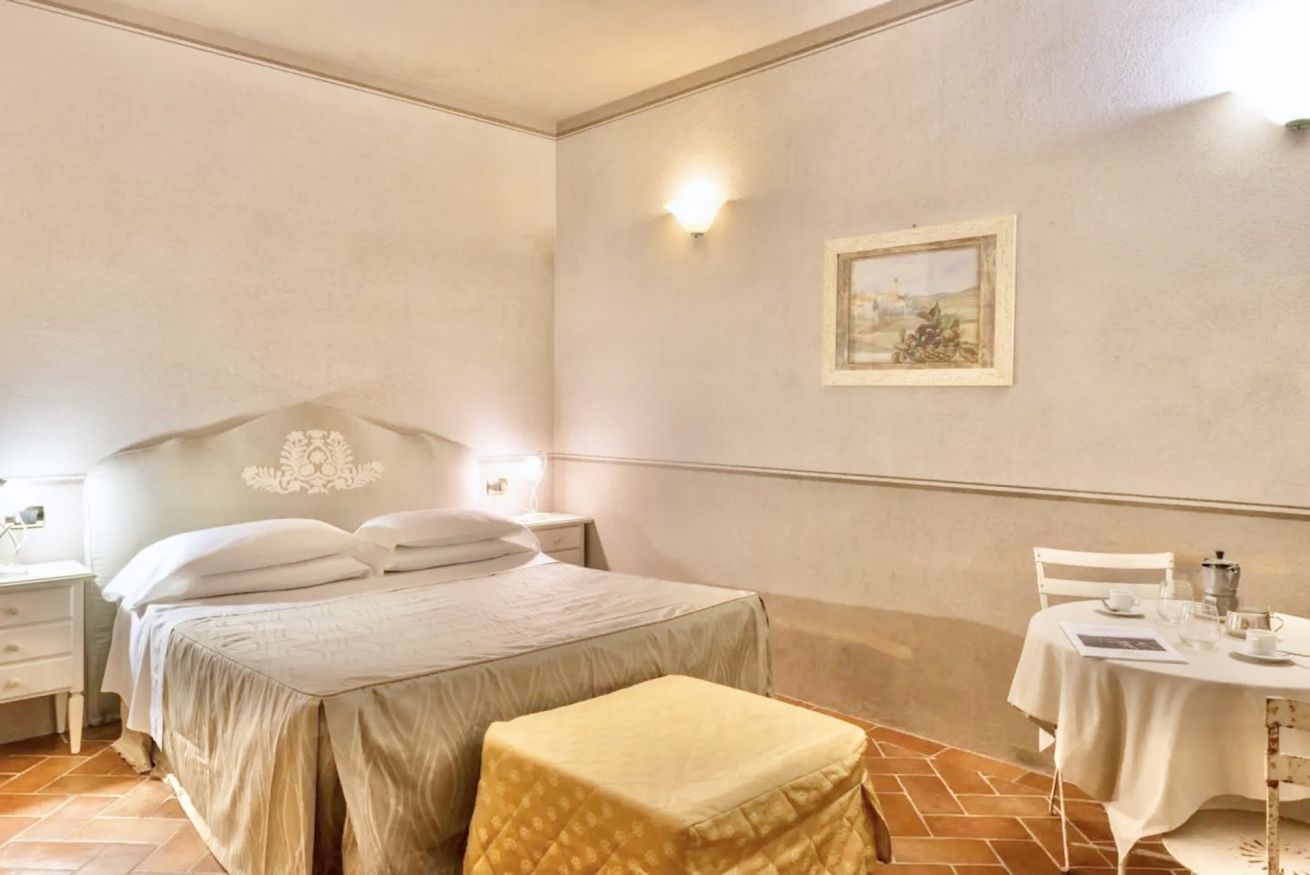 A bedroom with a bed, bedside table, nightstand, and a small table with a chair.