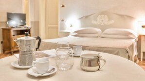 A neatly arranged breakfast table with a coffee maker, cups, and a pitcher, set against a bed and a television in a hotel room. - This studio apartment, approximately 23 square meters in size, sleeps two. It is tastefully furnished and air-conditioned. It features a kitchenette equipped with dishes, an oven, a refrigerator, satellite TV, a living room with a double bed, and a priva (Monteverdi Marittimo)