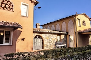 Ein Gebäude mit Stein- und Stuckfassade, Rundbogenfenstern und einer Terrasse mit Gartenmöbeln.