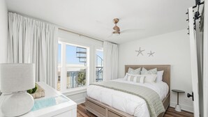 Ein Schlafzimmer mit Bett, Deckenventilator, Fenster mit Vorhängen und Blick auf Gebäude.