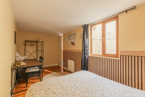 Une chambre à coucher avec un lit, un bureau avec une chaise, un radiateur et une fenêtre avec des rideaux.