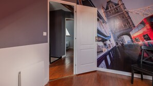 Une pièce décorée d’une fresque représentant un pont et une tour, dotée d’un plancher en bois et d’une porte blanche.