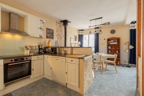 Une cuisine avec des meubles blancs, un four encastré, un lave-vaisselle et un coin repas comprenant une table et des chaises.