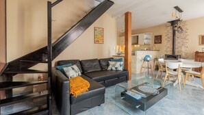 Un salon moderne avec un escalier noir, un canapé en cuir noir, une table basse en verre et un coin cuisine à l’arrière-plan.