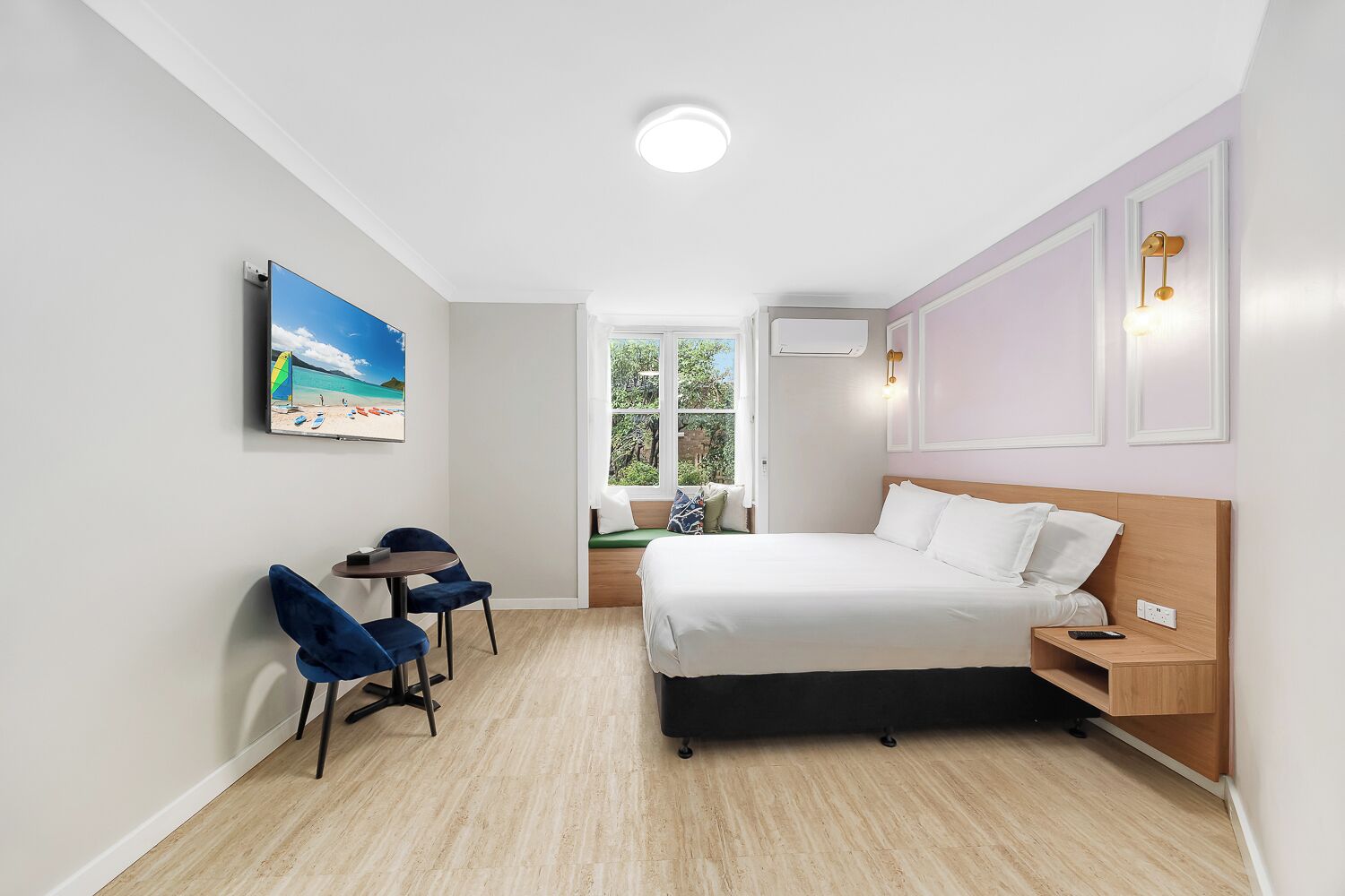 Ein Hotelzimmer mit Bett, Nachttisch, Stuhl, Schreibtisch, Fenster und einem Bild an der Wand.