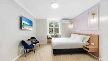 Ein Hotelzimmer mit Bett, Nachttisch, Stuhl, Schreibtisch, Fenster und einem Bild an der Wand.