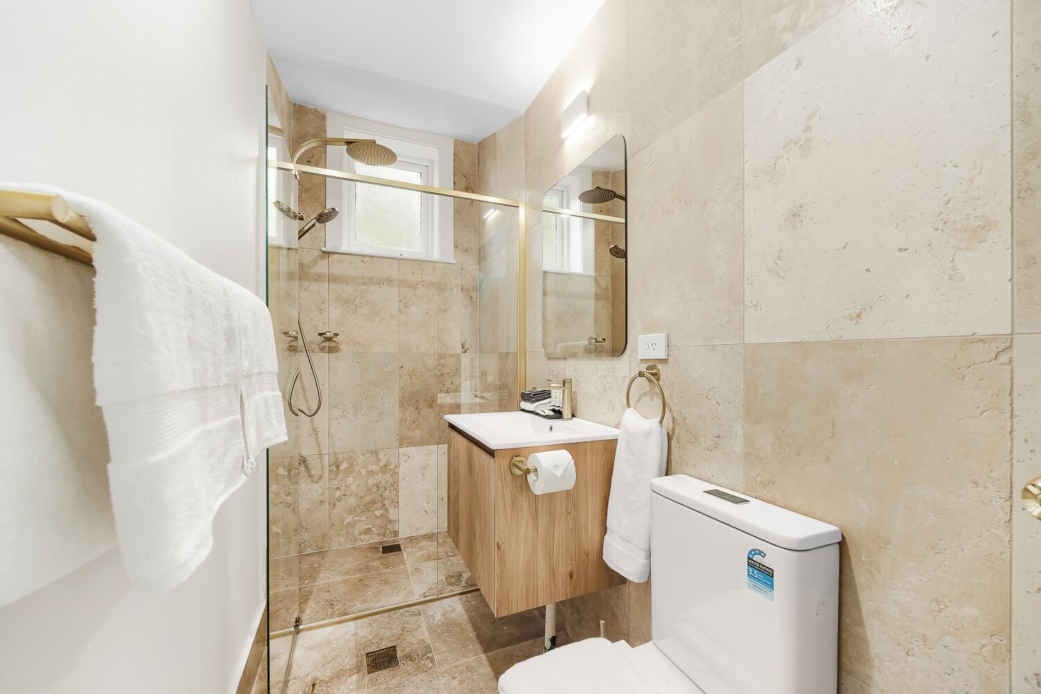 Ein Badezimmer mit Glasdusche, Holzwaschbecken, Toilette und Spiegel.