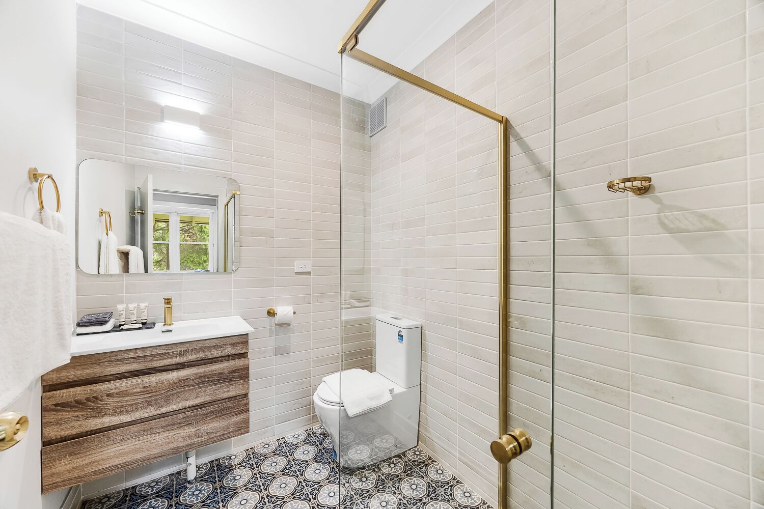 Een badkamer met witte metrotegels, een houten wastafelmeubel, een toilet en een douchecabine met glazen wanden.