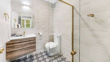 A bathroom with white subway tiles, a wooden vanity, a toilet, and a glass shower enclosure.