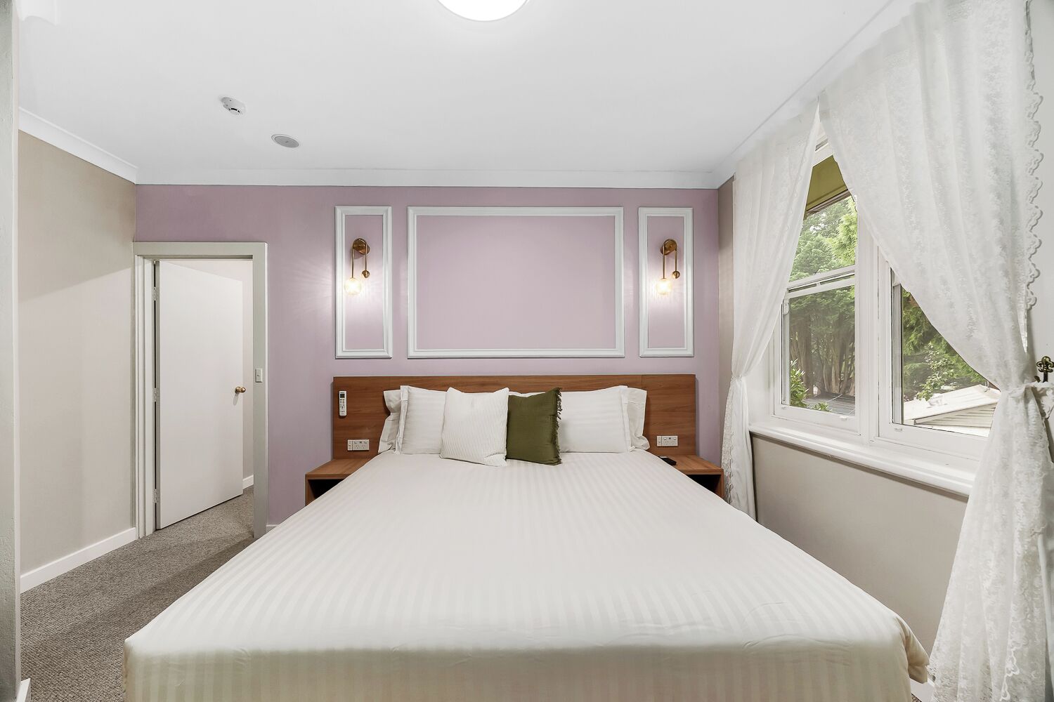 A bedroom with a bed, nightstands, a window with curtains, and wall-mounted lighting.