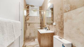 Un baño con ducha de vidrio, tocador de madera, lavabo blanco y espejo.