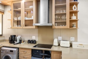 A modern kitchen with wooden cabinets, a stainless steel range hood, a built-in oven, a coffee machine, a toaster, and a bread box. - Kiahuna 2 (uMhlanga)