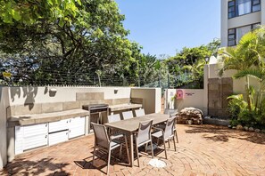 An outdoor patio with a barbecue grill, dining table, and chairs. - Kiahuna 2 (uMhlanga)