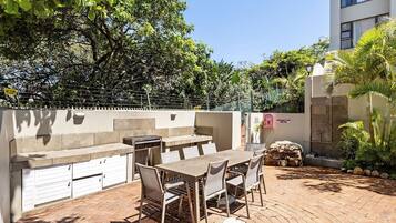 An outdoor patio with a barbecue grill, dining table, and chairs.