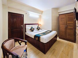 Ett hotellrum med en säng, en garderob i trä, en stol och en tv.