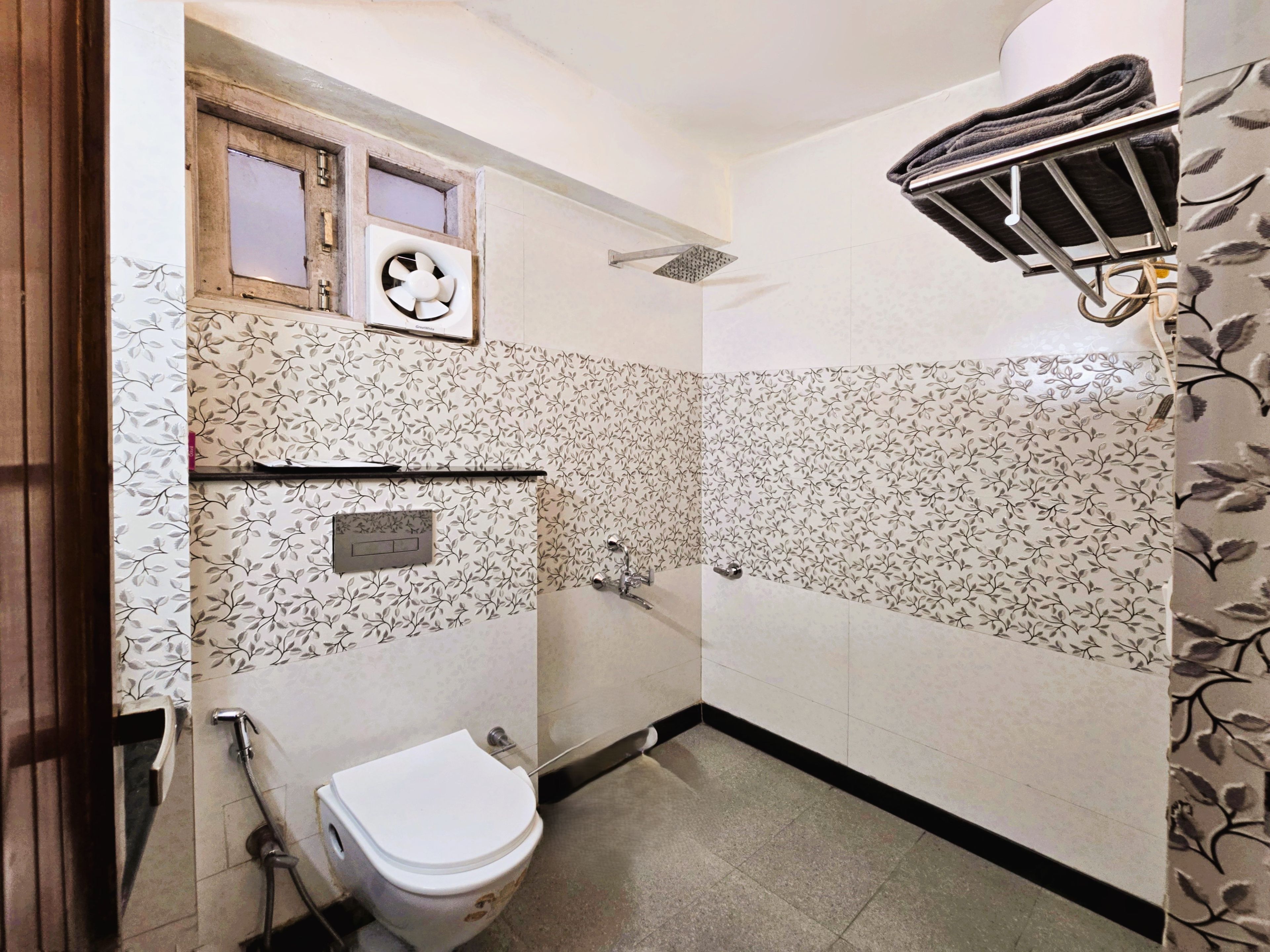 A bathroom with a toilet, a shower, a towel rack, and a window.