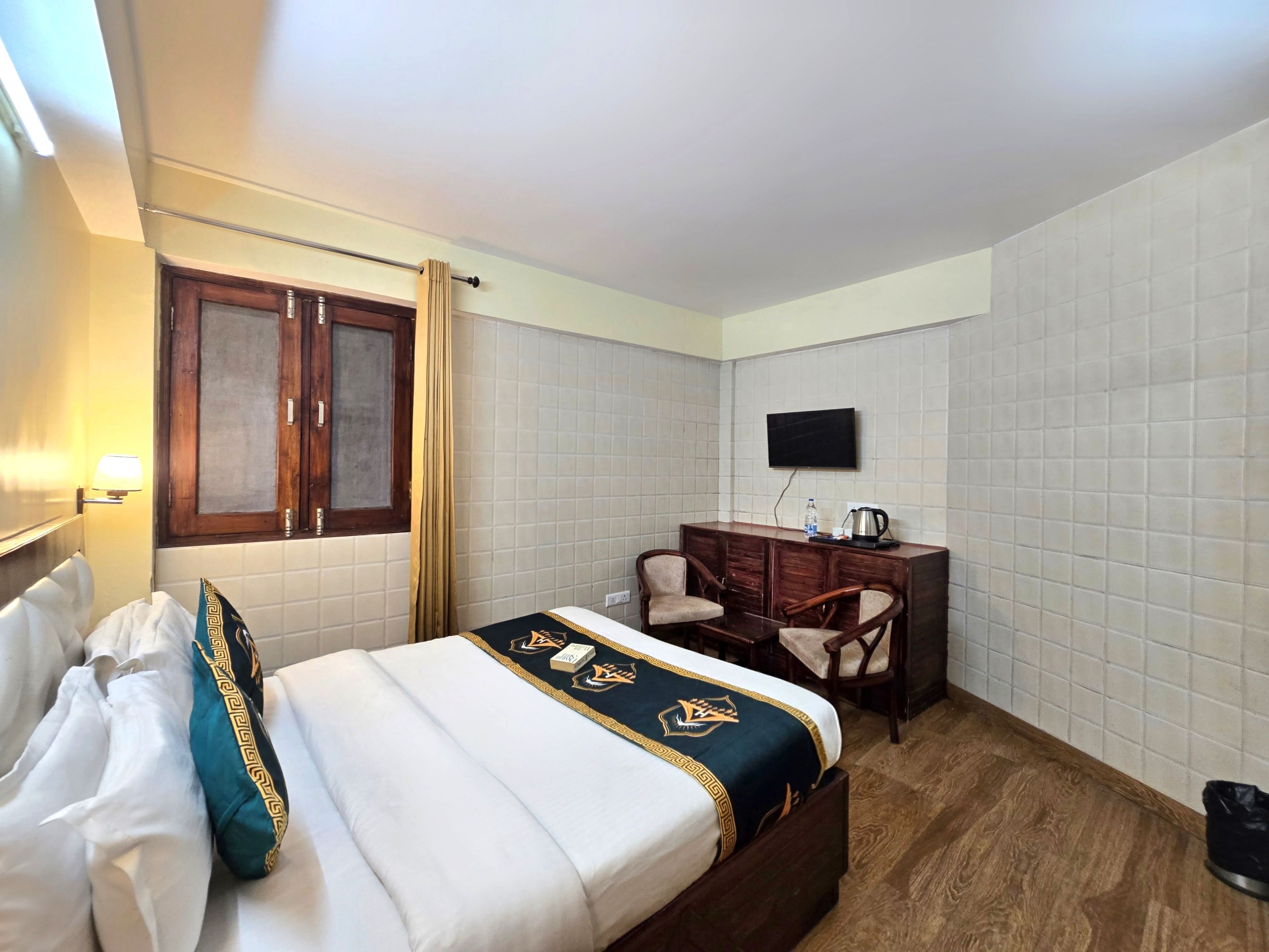 A hotel room with a bed, a desk, a chair, a television, and a window with curtains.