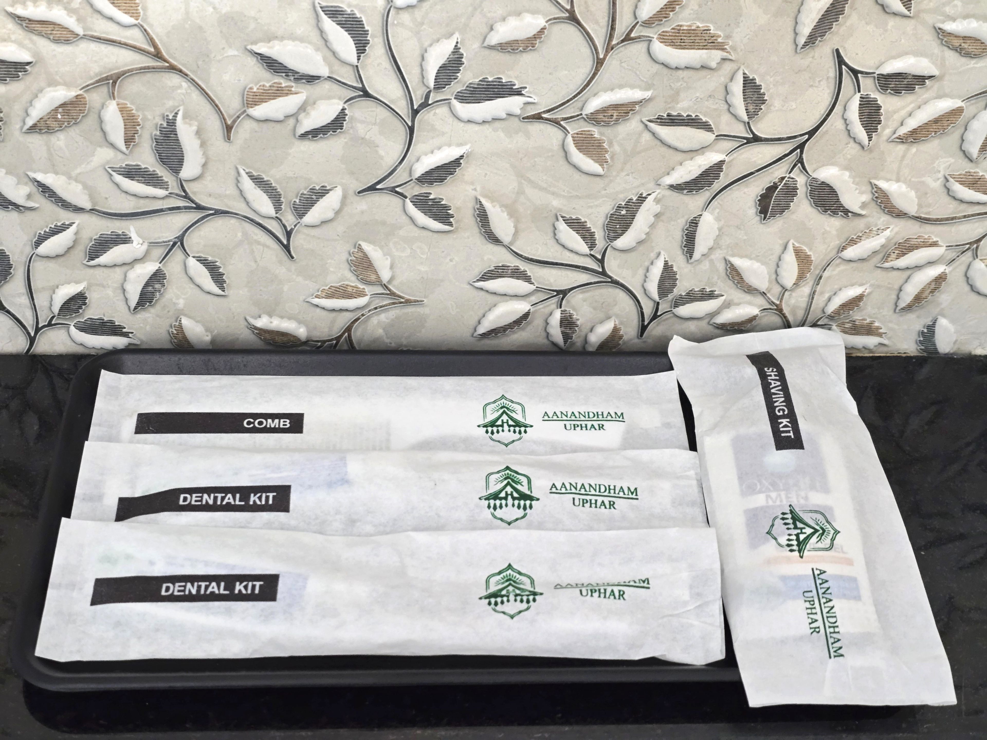 Un plateau noir contenant des trousses de soins dentaires et des trousses de rasage, le tout posé sur un fond de papier peint à motifs floraux.