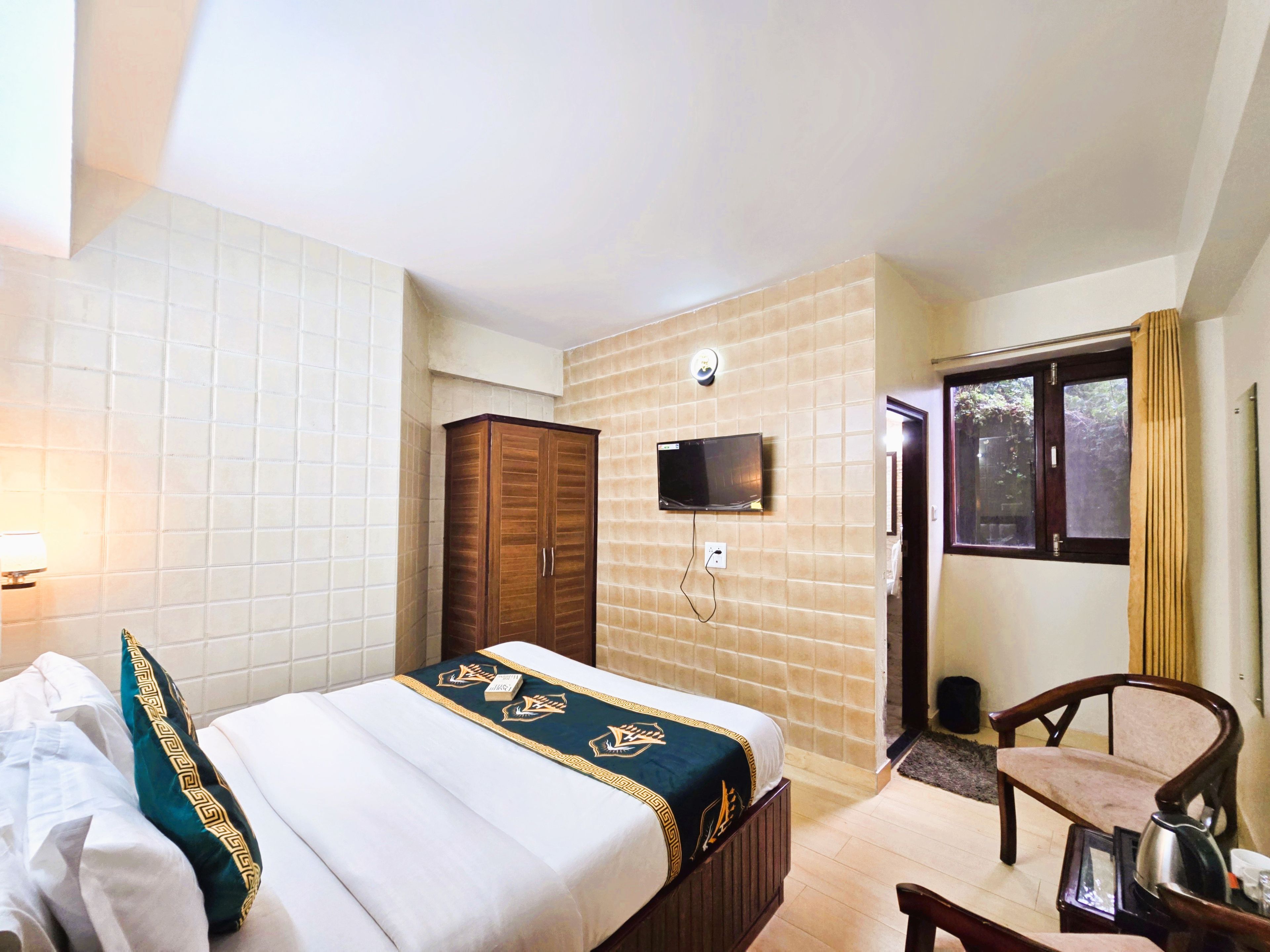 Une chambre d’hôtel avec un lit, un téléviseur fixé au mur, une armoire et une fenêtre avec des rideaux.