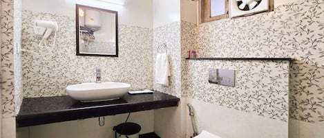 Une salle de bain avec un lavabo, un miroir et des toilettes blancs. Il y a une fenêtre avec un ventilateur au-dessus des toilettes.