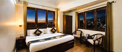 A hotel room with a large bed, a desk, two chairs, and a view of the city at night.