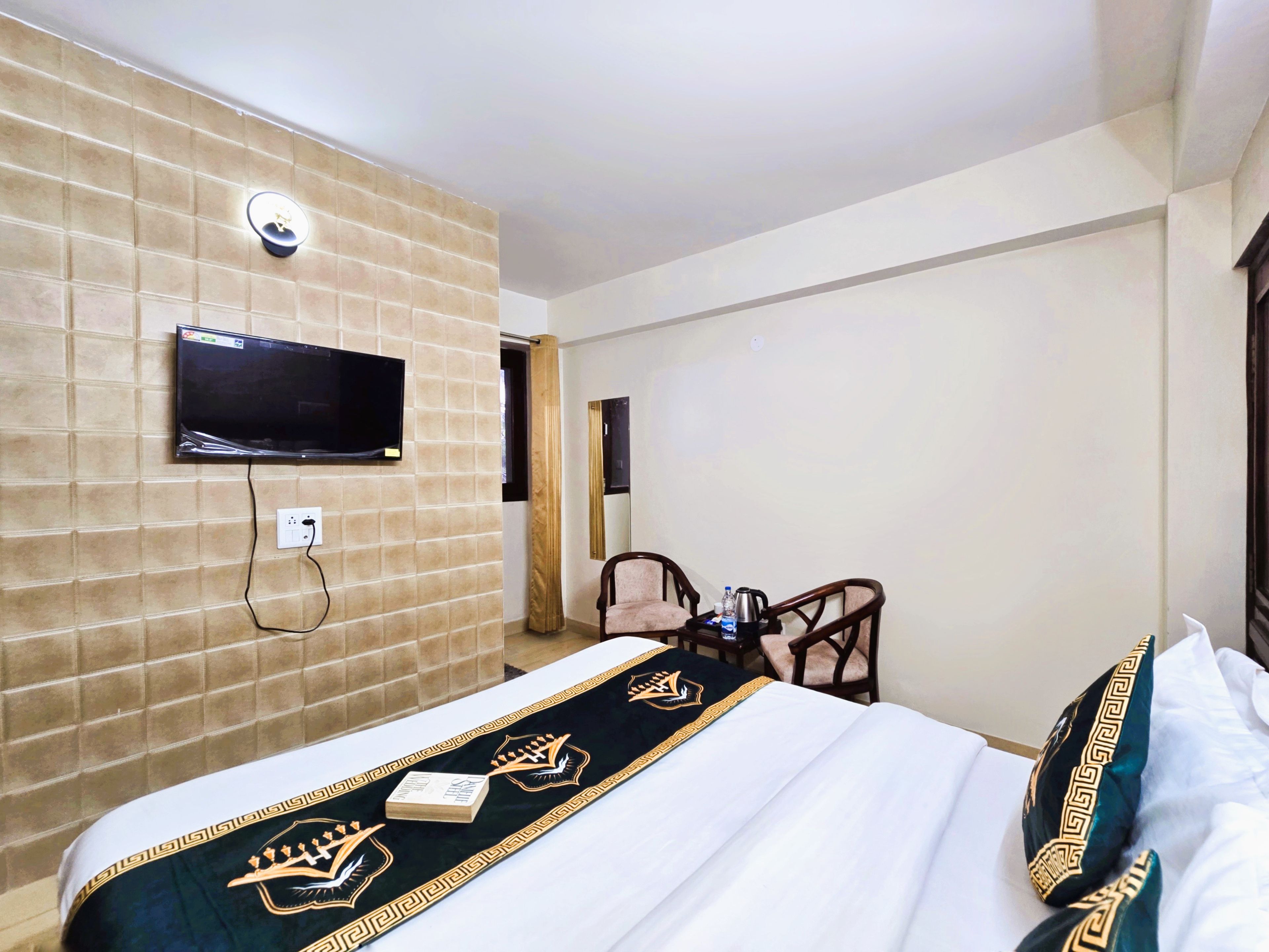 Ein Hotelzimmer mit einem Bett, einem an der Wand befestigten Fernseher, einem Schreibtisch mit Stuhl und einem Fenster.