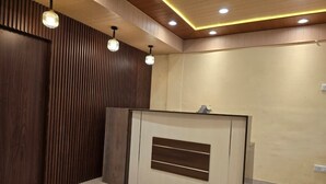 A reception area with a wooden panel wall, a reception desk, and pendant lighting. - Kavin Uphar - The Mall (Shimla)