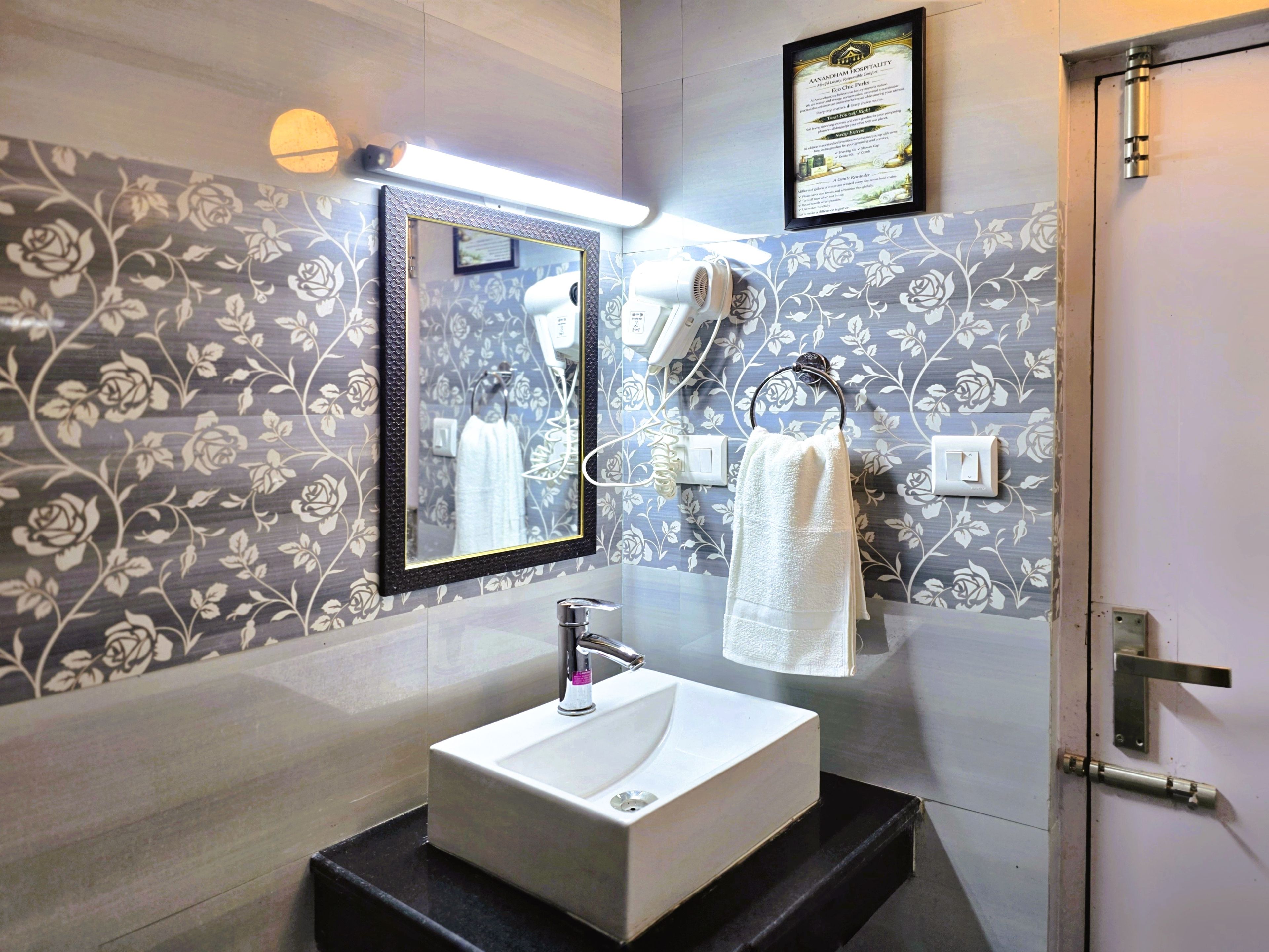 Une salle de bain avec un lavabo blanc, un miroir, un porte-serviettes et un sèche-cheveux fixé au mur.