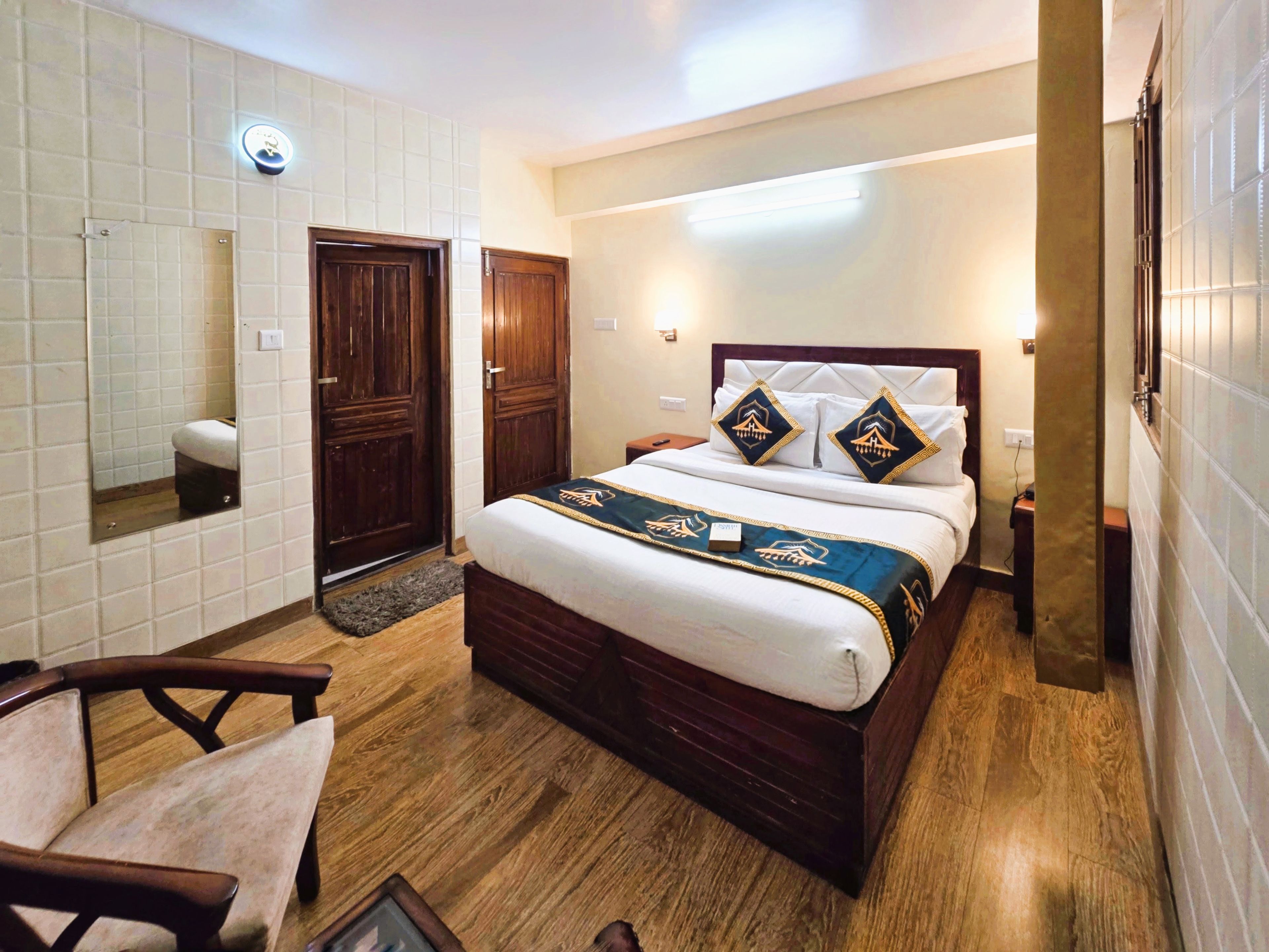 A hotel room with a wooden bed, a bedside table, a chair, and a large mirror.